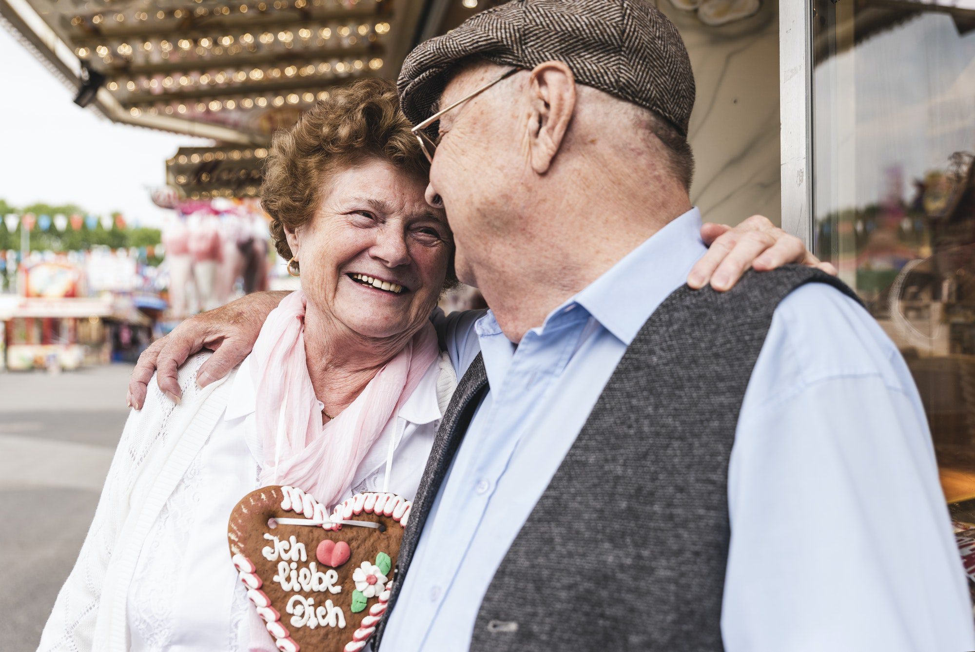 Happy senior couple with gingerbread heart at fair discussing their new 2022 Medicare Part C and D costs.